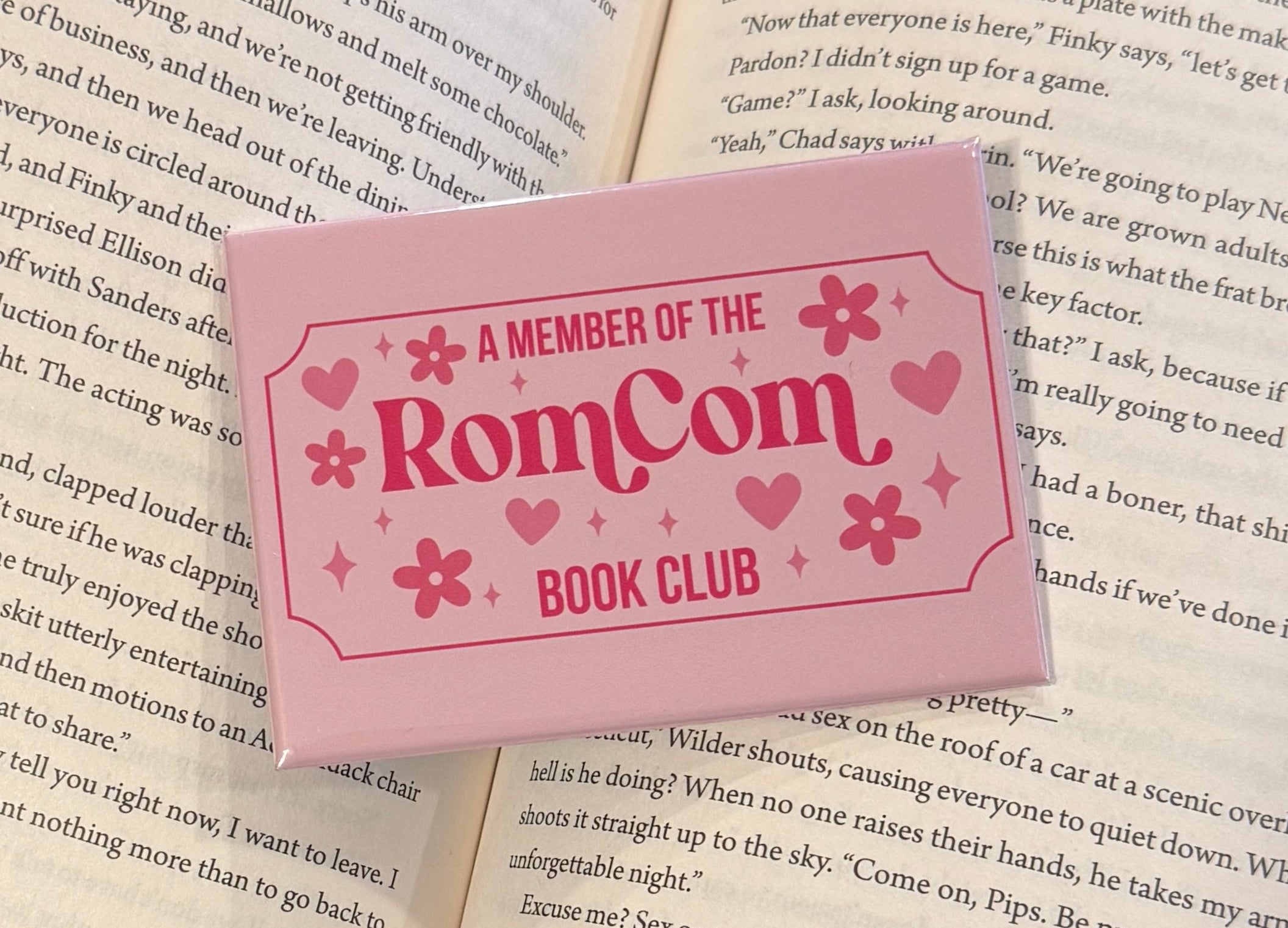 Open book with a pink magnet reading 'A Member of the RomCom Book Club' on a hardback fridge magnet.
